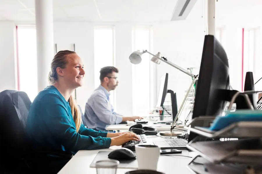 Work at computer desks in a modern office, focus on the person in front.