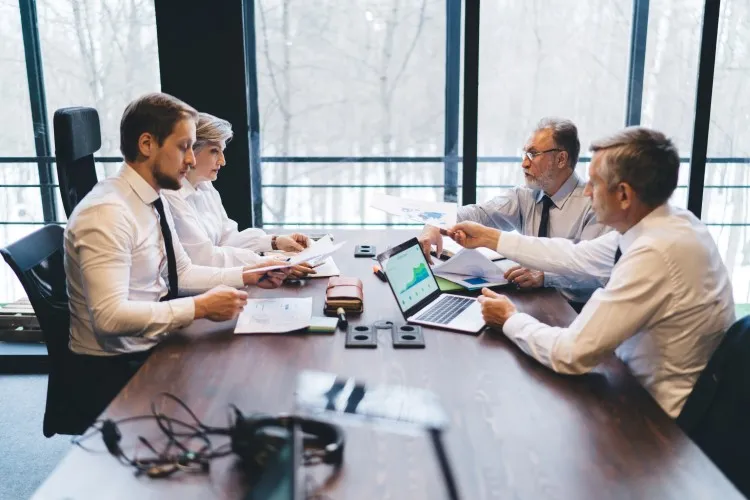 Board at a meeting: several managers at the table discuss documents and charts, on the table a laptop.
