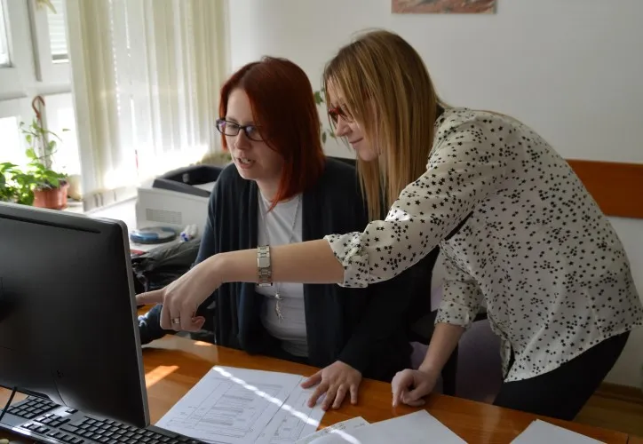 Two female clerks working at a computer in a public administration office; documents on the desk.