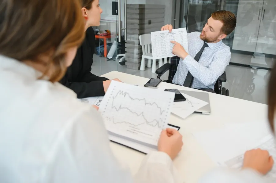 The finance team discusses printouts with charts at the table; a man points to a data sheet.
