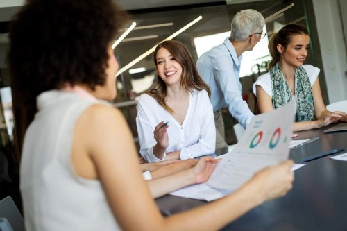 The team meeting at the table; the woman in the foreground holds the chart report, the rest talk and smile.