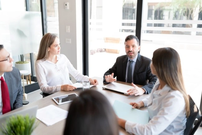 Business meeting in a glassed-in office — the team leader discusses the topic, four people at the table.