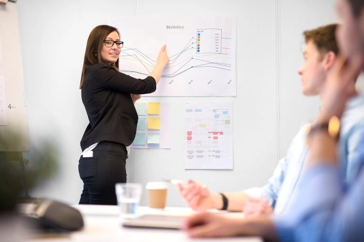 Analysis of the results: graphs on the wall, a woman translates data, on the table notes and cups.