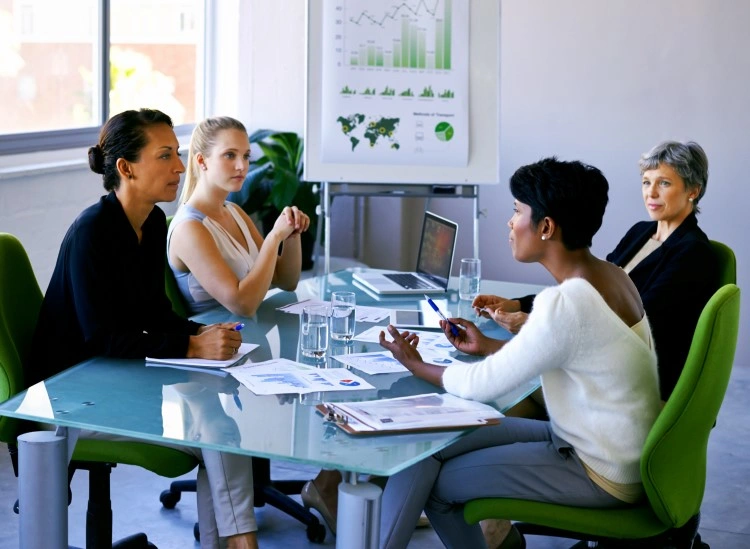 Data analysis in the office: conversation at the table with documents, laptop and flipchart in the background.