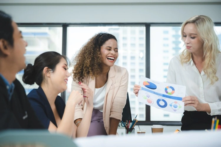 Brainstorming in a bright office — a person shows an infographic sheet, a group engaged in conversation.
