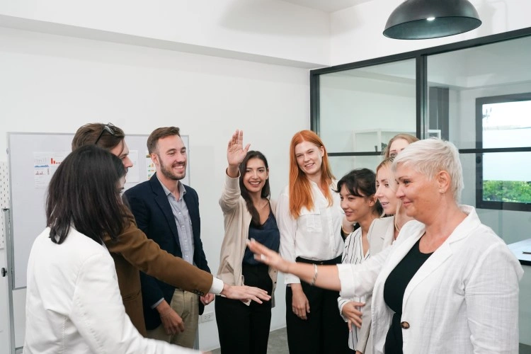 Team meeting in a glazed office: nine people, hands outstretched to a common shout.