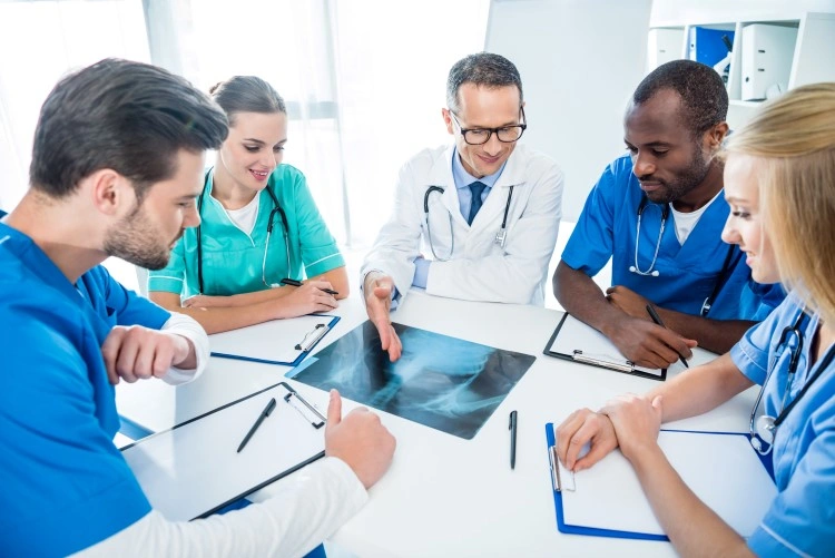 The medical team discusses the diagnosis — the doctor points to the X-ray film, the others listen.