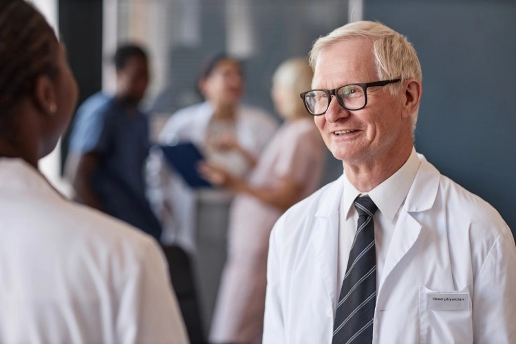 An experienced medic in glasses smiles during a conversation, behind him a movement in the staff zone.
