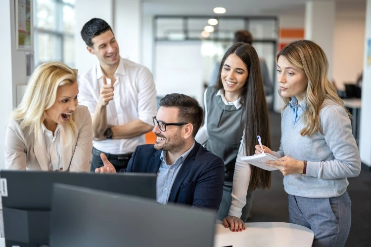 Success of the project: colleagues smile, looking at the screen, one person holds a notebook.