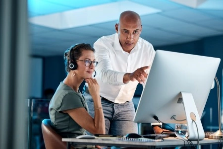 Specialists at the computer in the office: a man points to a monitor, a woman in headphones analyzes the data.
