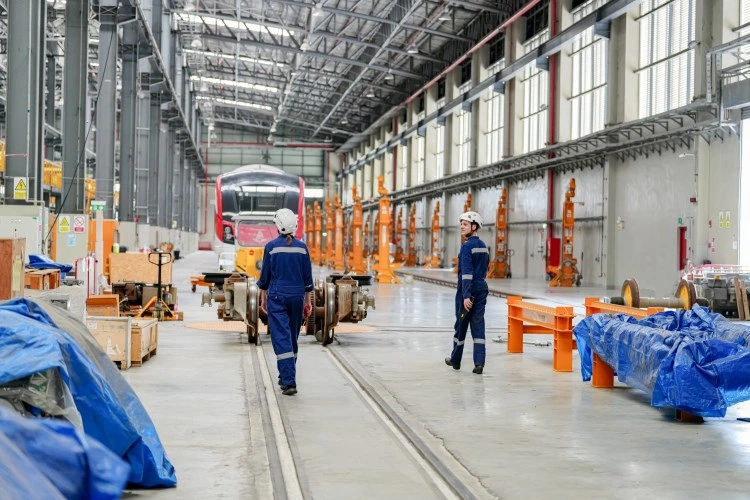 Large factory — assembly line, trolleys and blue tarpaulin elements, staff in workwear.