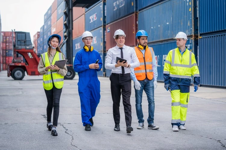 Logistics team during the celebration: various roles, health and safety equipment, background with colorful containers.