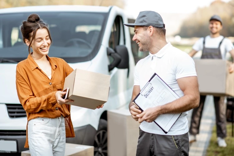 Delivery scene: exchange of the package in front of the courier car, in the background the helper carries the carton.