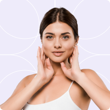 A woman with brown hair and green eyes is holding her face with both hands. She is wearing a white tank top. The background is light purple with white circles.