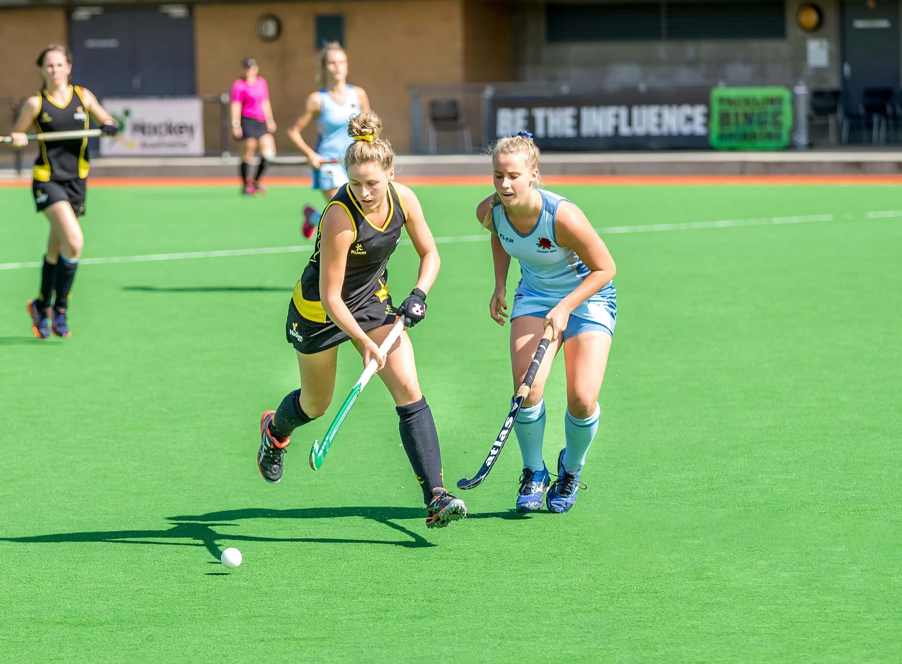 Two women playing field hockey, running on the pitch.