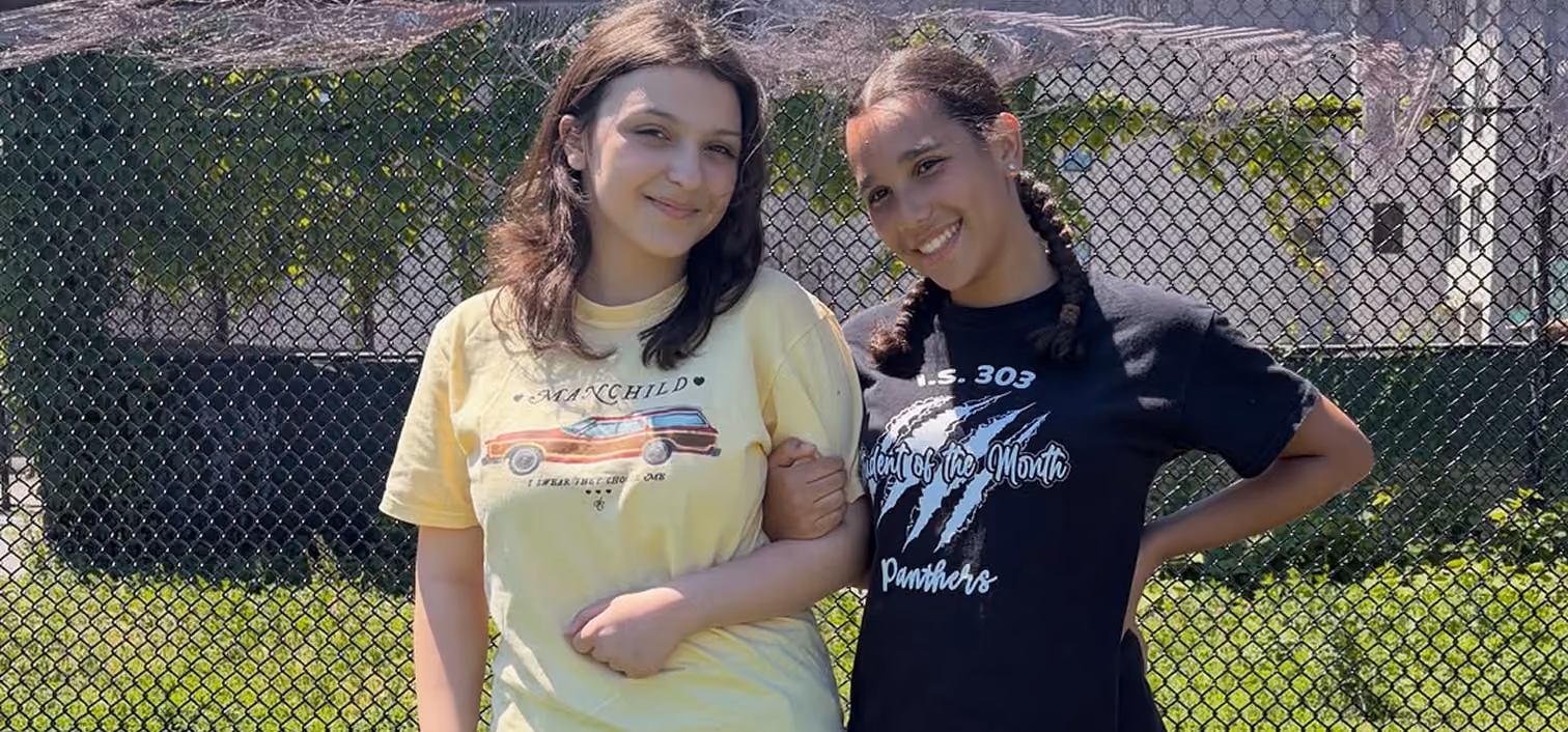 Two IS 303 students smiling outdoors, one wearing Student of the Month shirt
