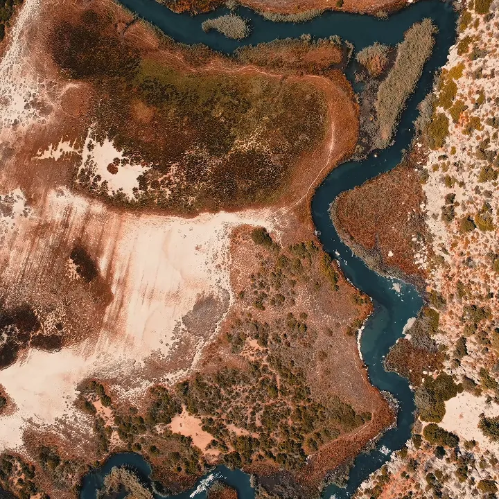 Aerial view of a winding river surrounded by dry, patchy vegetation and sandy areas.