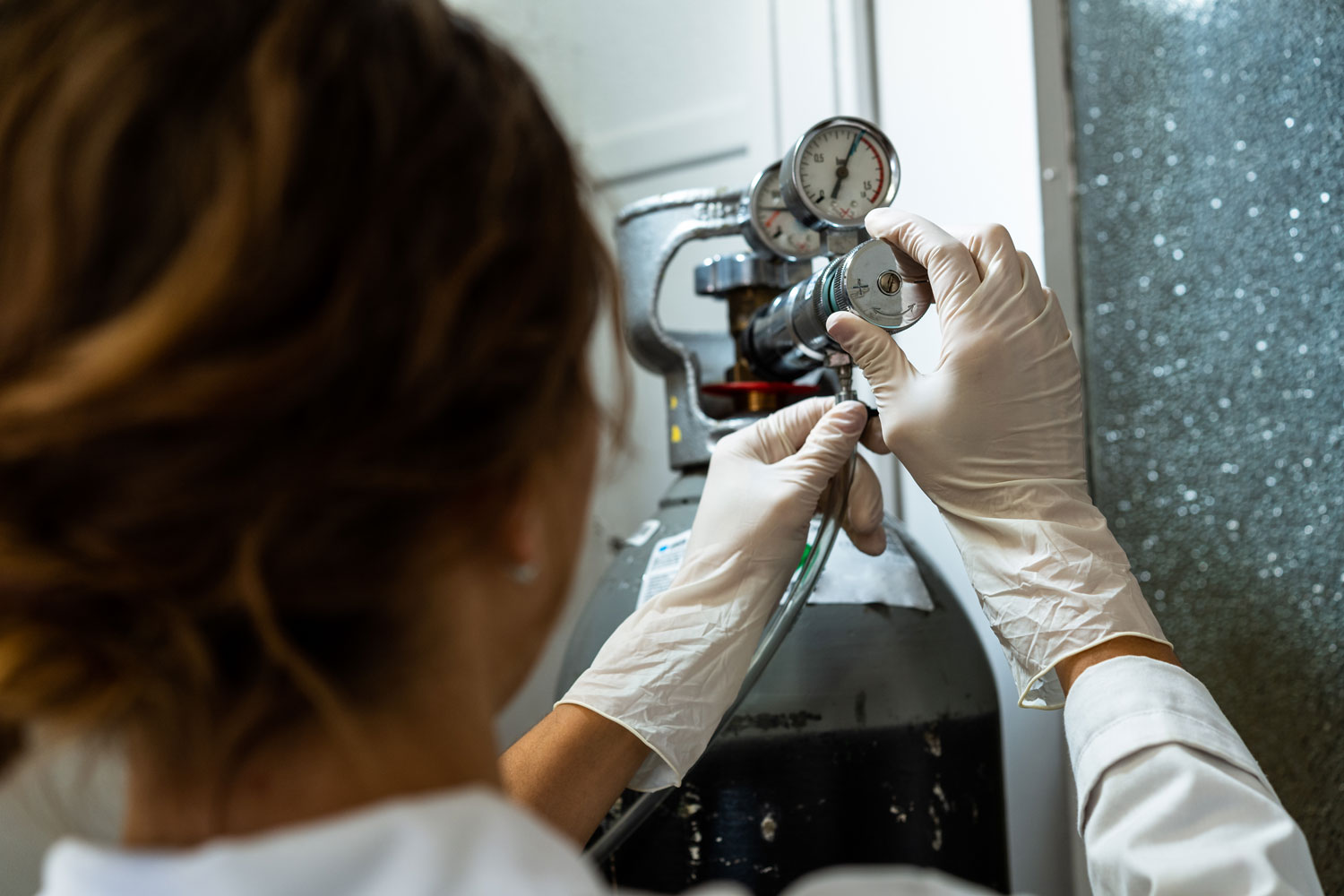 Person wearing white gloves adjusting pressure gauge on a gas cylinder.