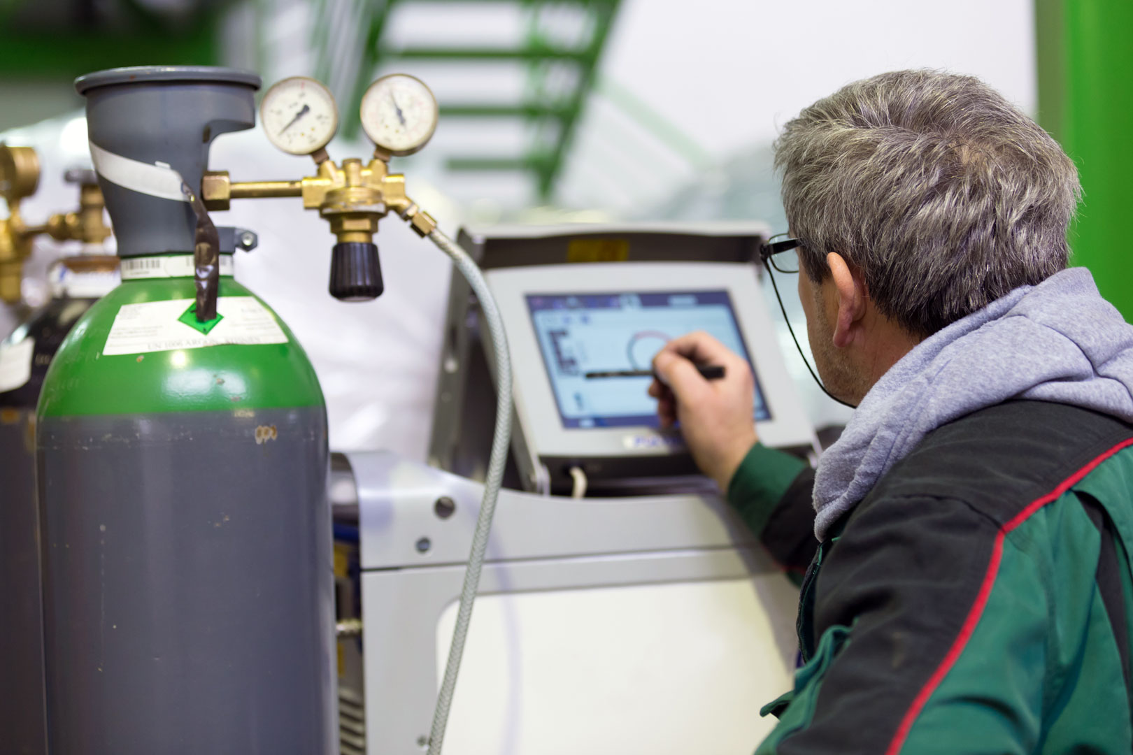 Technician adjusting settings on a touchscreen device next to a gas cylinder with pressure gauges.