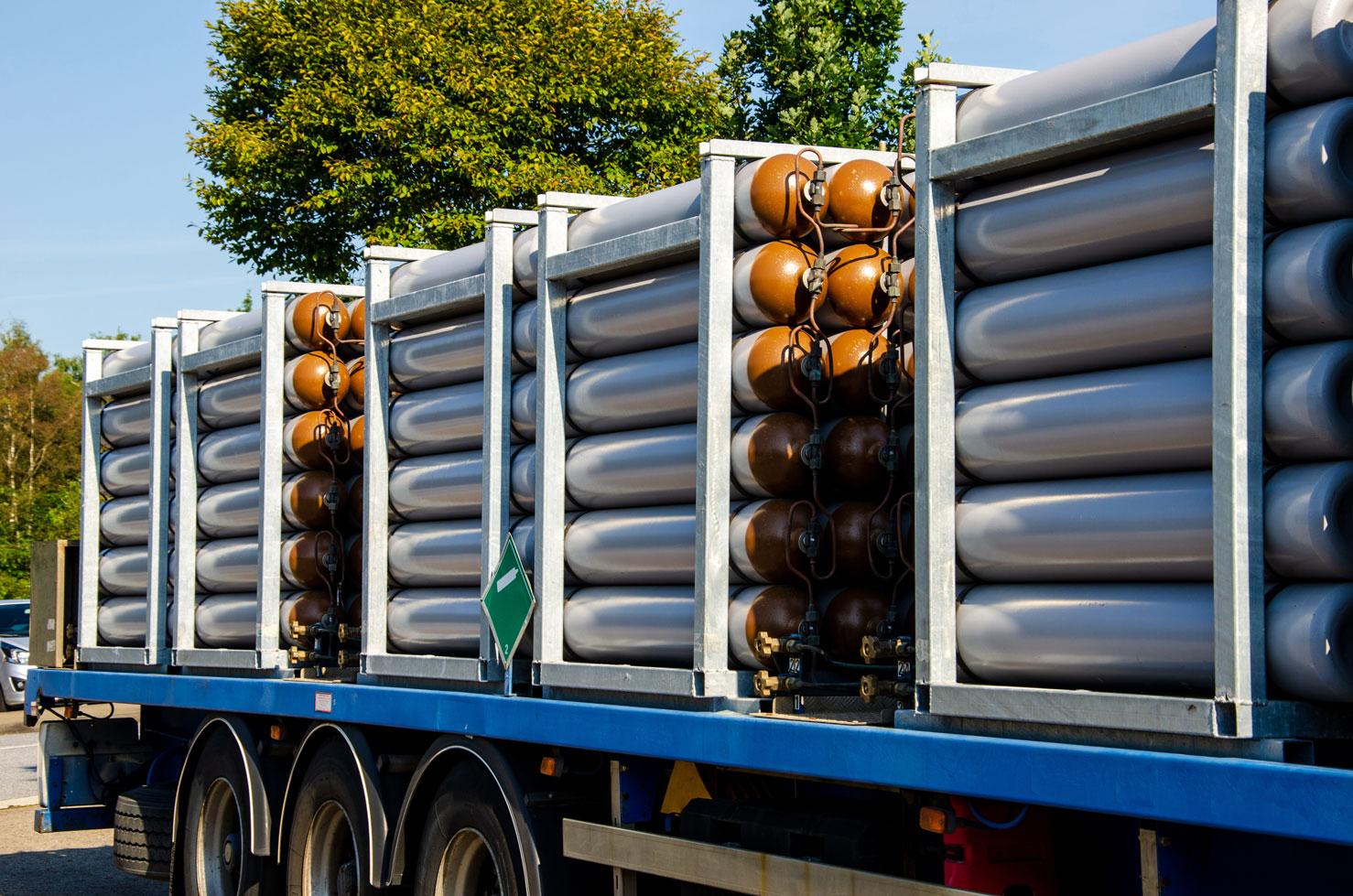 Flatbed truck loaded with multiple large industrial gas cylinders secured in metal frames.