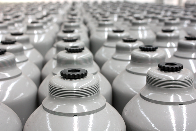 Rows of closely packed white industrial gas cylinders with black valve tops.