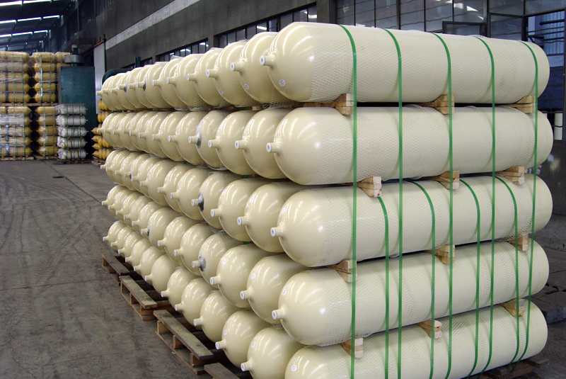 Stack of large beige industrial gas cylinders secured with green straps inside a warehouse.