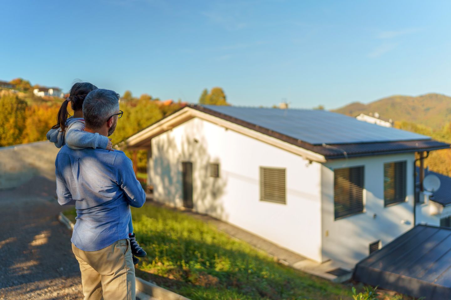 Mann mit Kind im Arm vor dem Haus mit Photovoltaikanlage