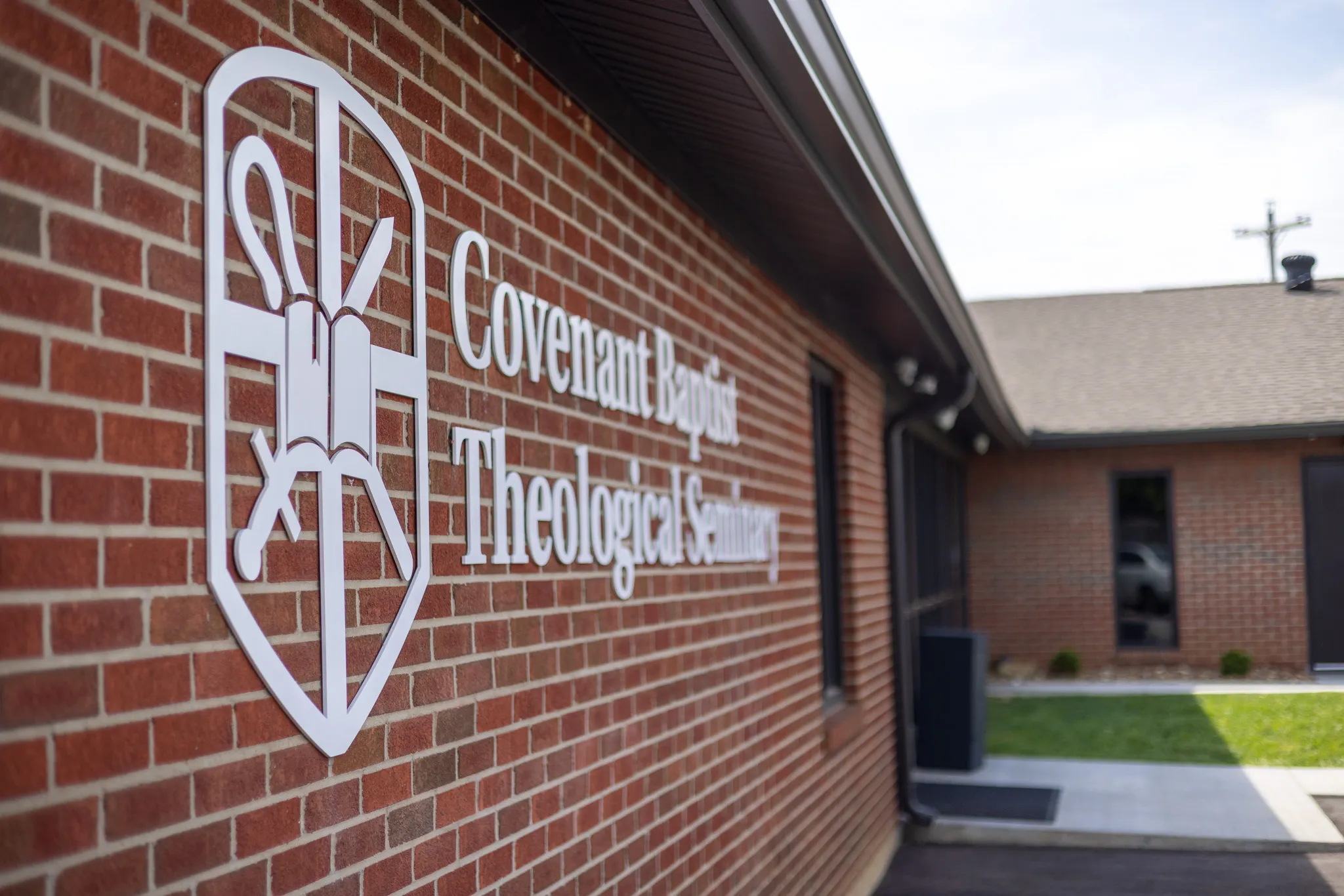 White sign with shield emblem and text 'Covenant Baptist Theological Seminary' mounted on a red brick building exterior.