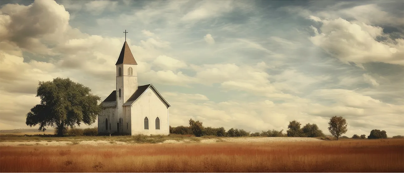 White church with a steeple and cross standing in an open field with tall grass under a cloudy sky.
