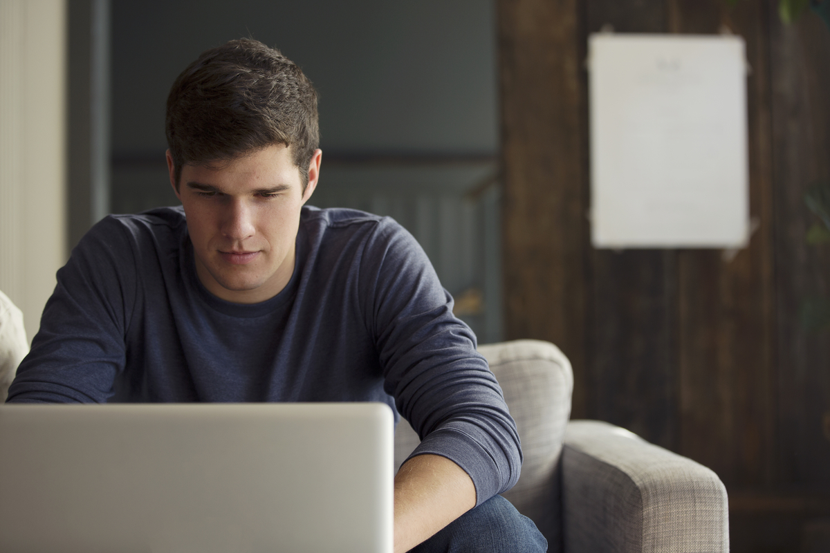Young man sitting on a couch and focusing on a laptop in front of him.