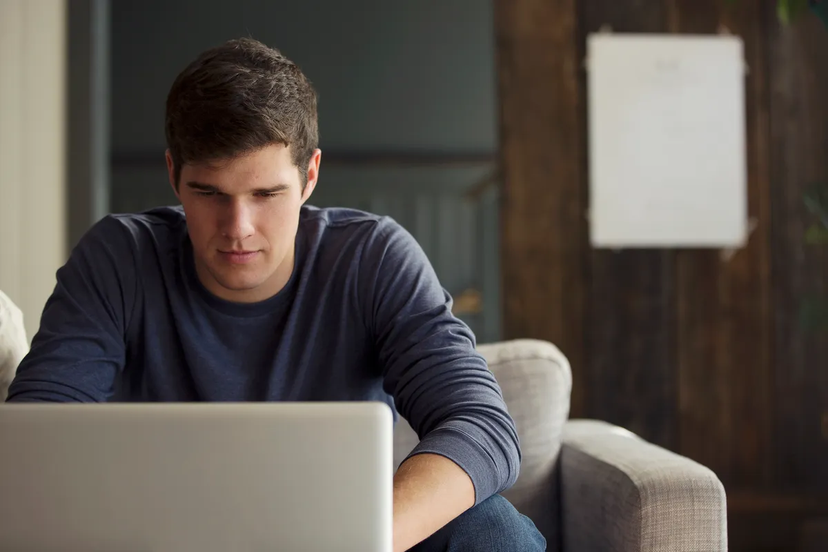 Young man sitting on a couch and focusing on a laptop in front of him.