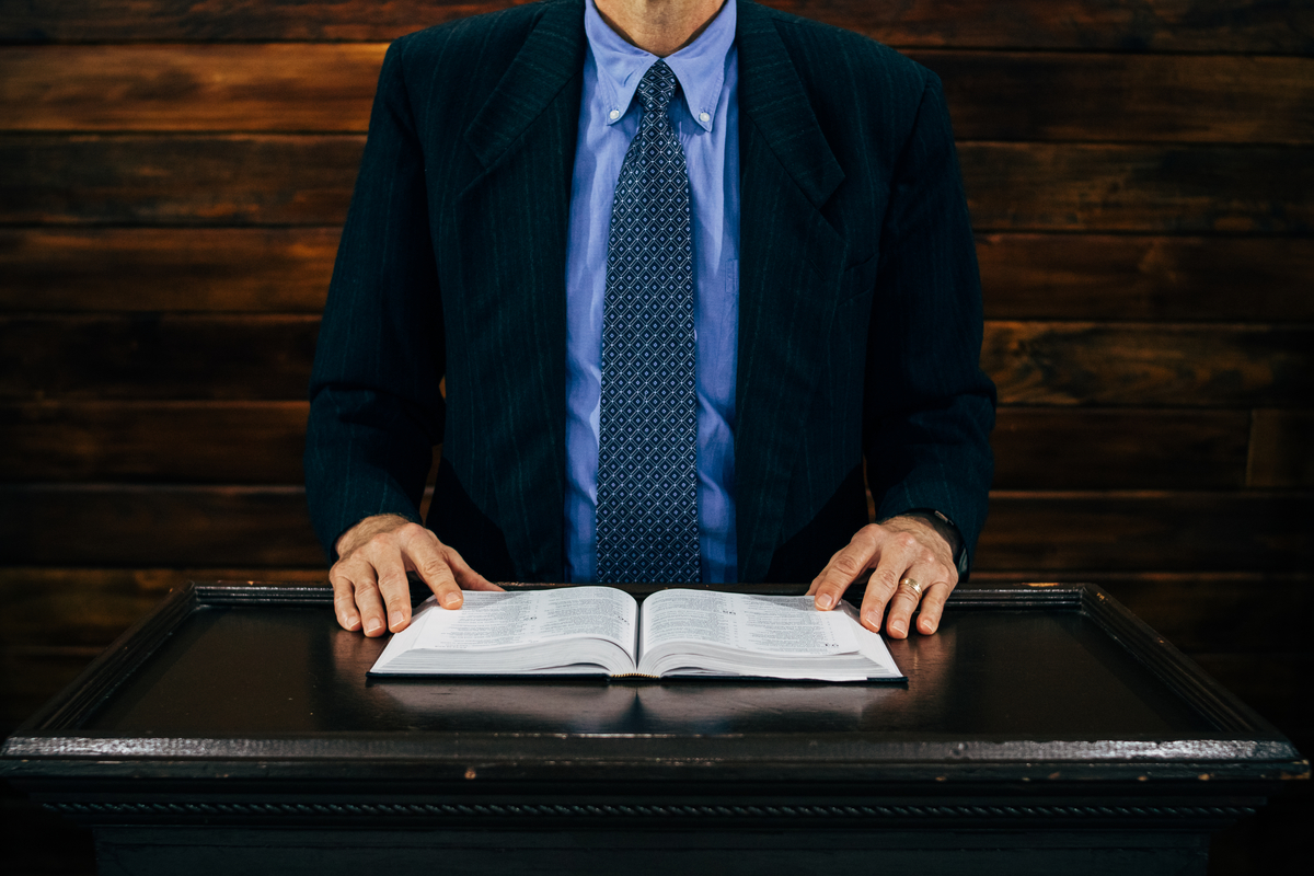 Man in a suit and tie standing behind a lectern with an open book.