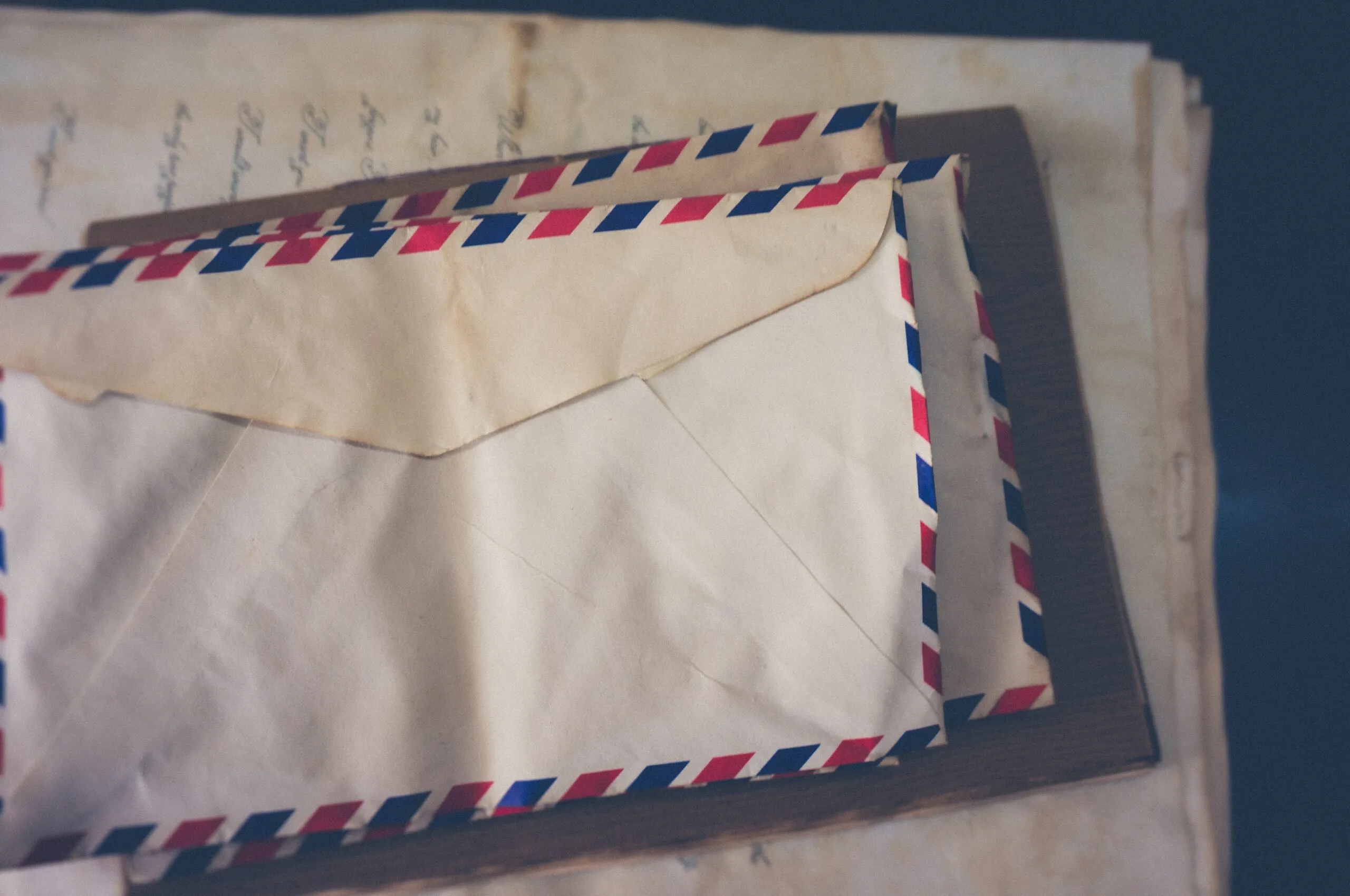 Stack of vintage airmail envelopes with red and blue striped borders on top of old handwritten letters.