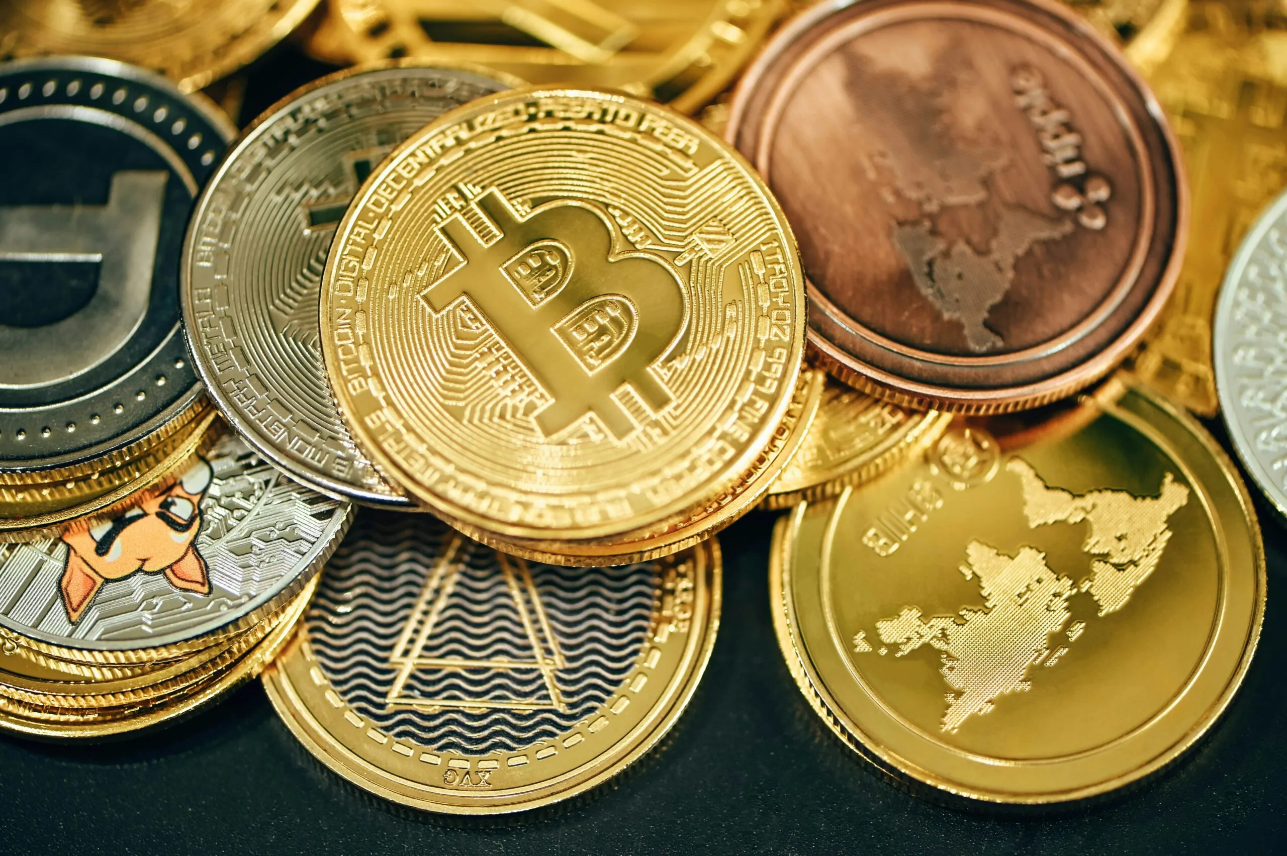 Close-up of various physical cryptocurrency coins including Bitcoin and others on a dark surface.