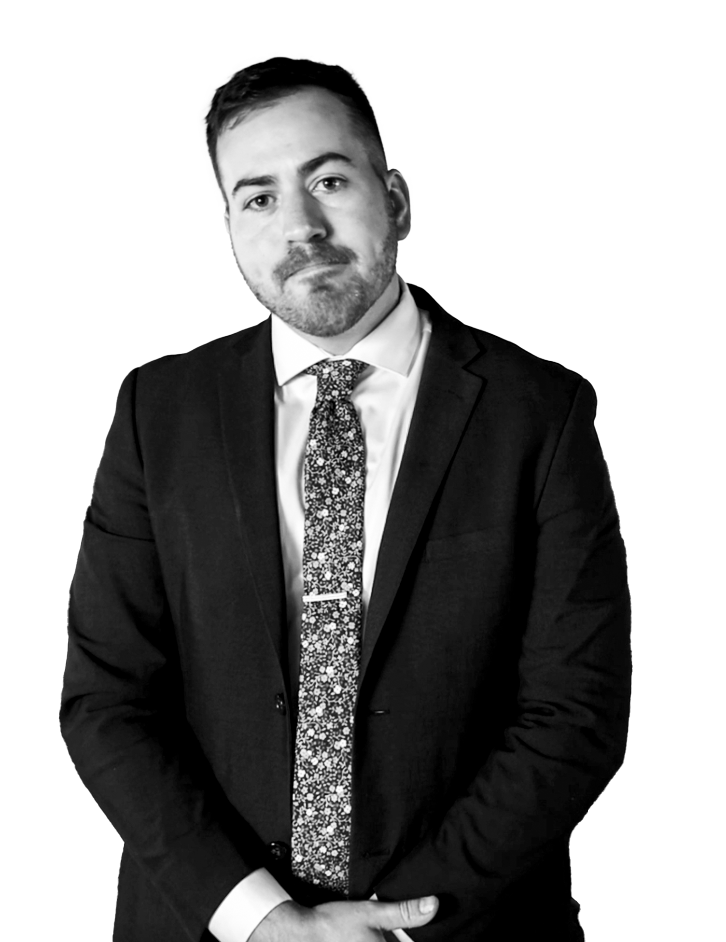 Man in suit with patterned tie standing with hands clasped, looking at the camera.