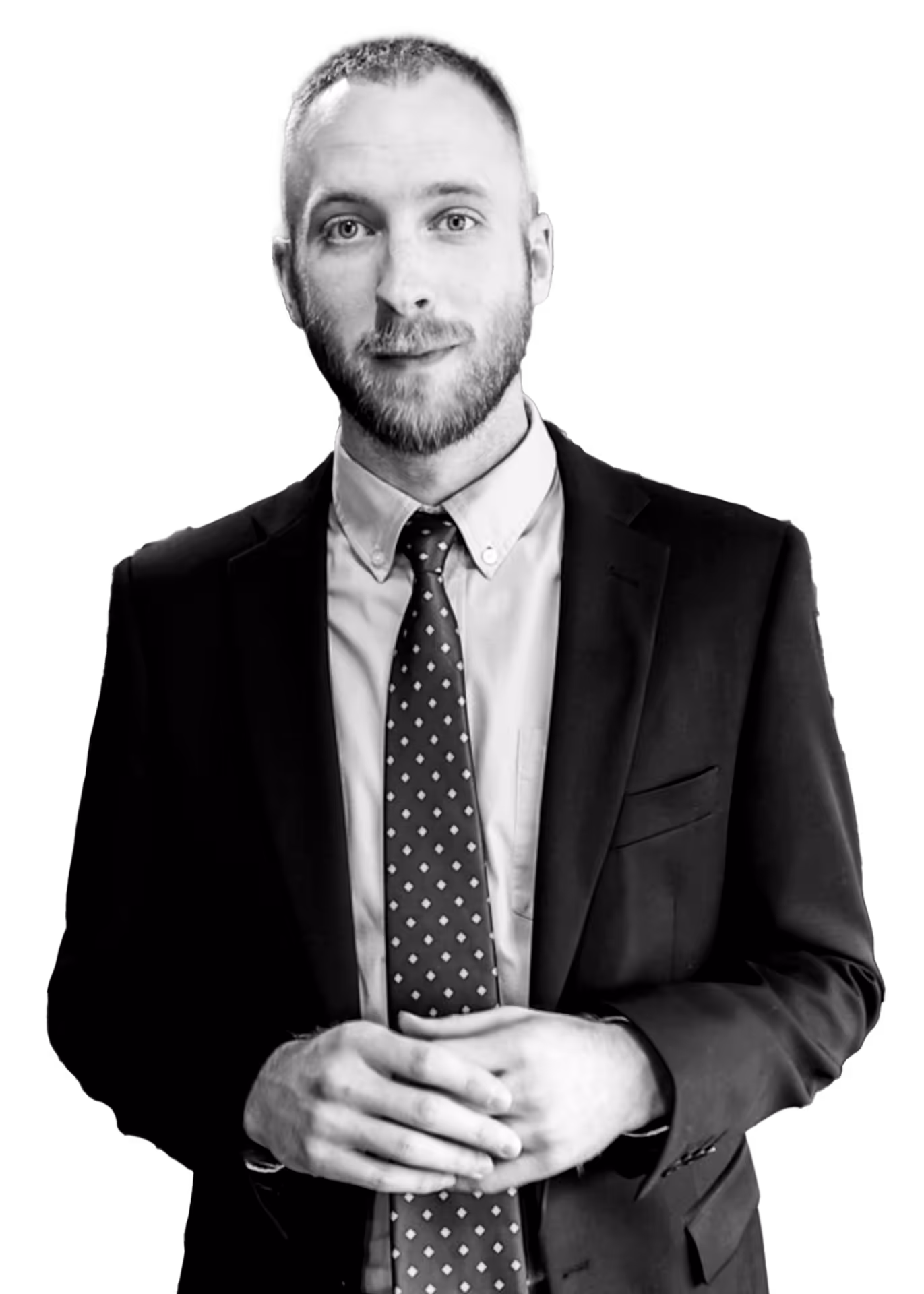 Man with a beard wearing a suit and patterned tie, posing with hands clasped.