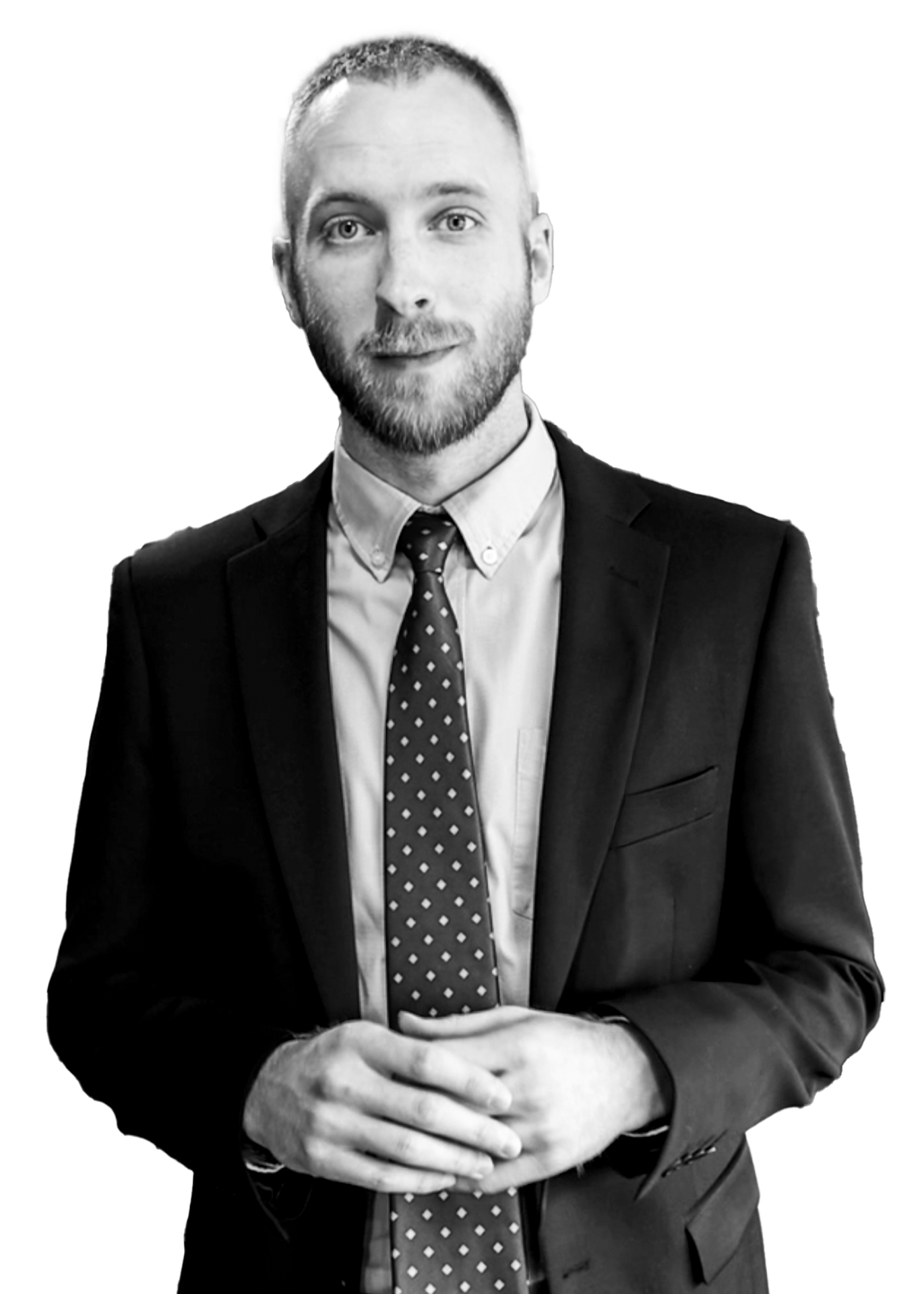 Man with a beard wearing a suit and patterned tie, posing with hands clasped.