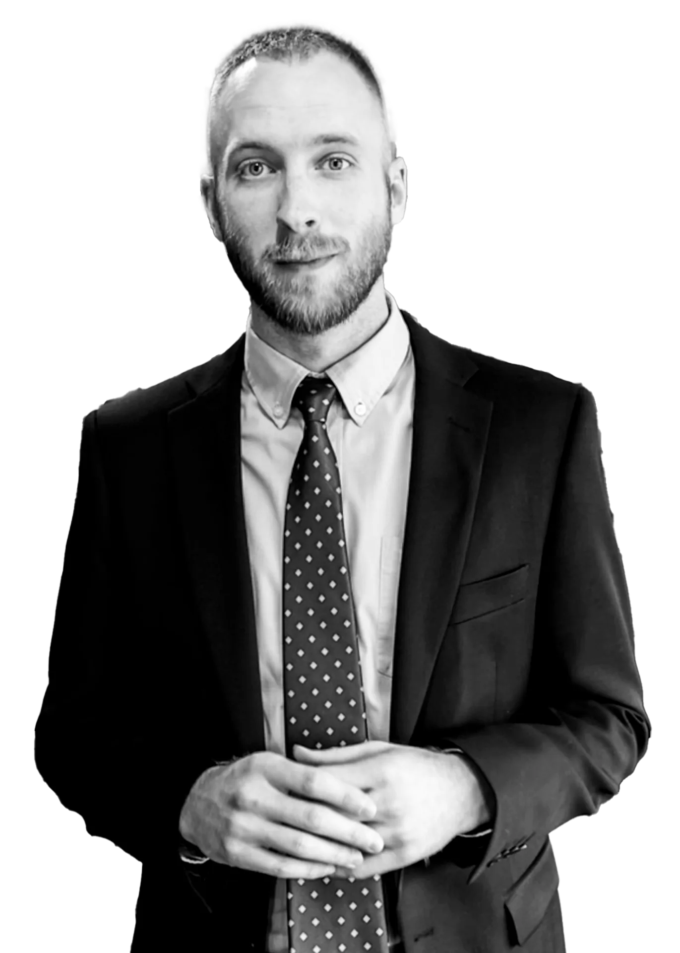 Man with a beard wearing a suit and patterned tie, posing with hands clasped.