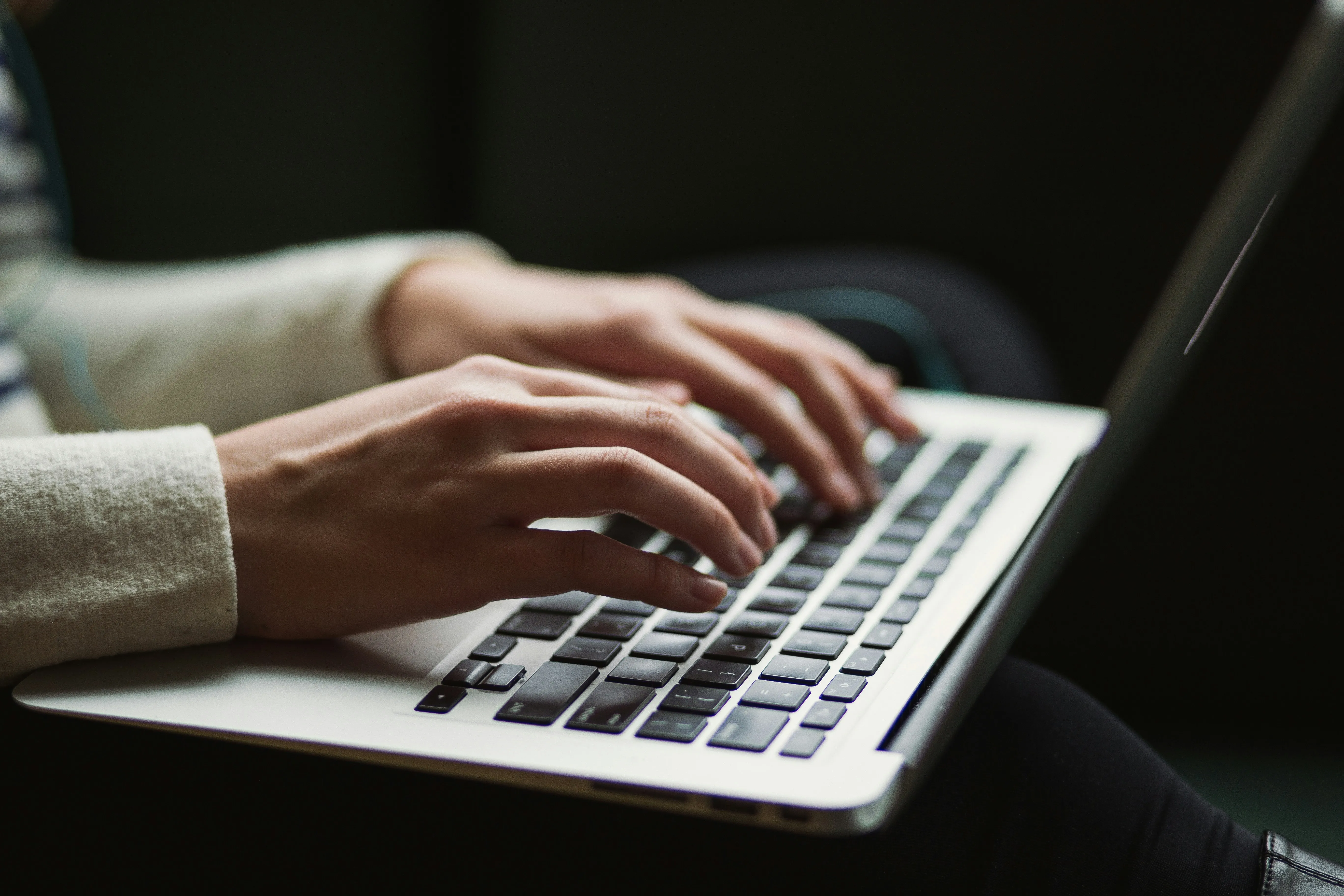 Close-up of hands typing on a laptop keyboard in a dimly lit environment.