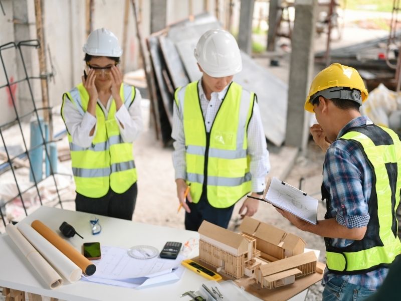 Equipo de construcción revisando planos y una maqueta de proyecto en obra para coordinar actividades