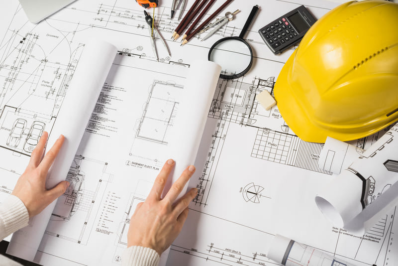 Planos arquitectónicos, casco de seguridad y herramientas de medición sobre una mesa de trabajo para la planeación, revisión y control técnico de proyectos de construcción con Diazar.