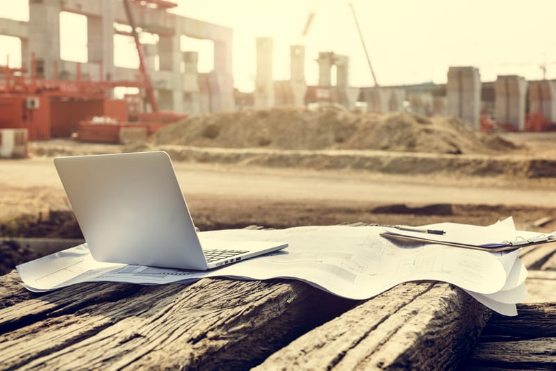 Laptop y planos colocados frente a una obra en construcción para consultar información, revisar avances y apoyar la planeación y gestión del proyecto con Diazar.