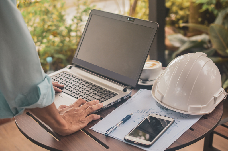 Profesional trabajando en una laptop junto a casco, planos y notas técnicas para consultar información y apoyar la planeación y administración de proyectos de construcción con Diazar.