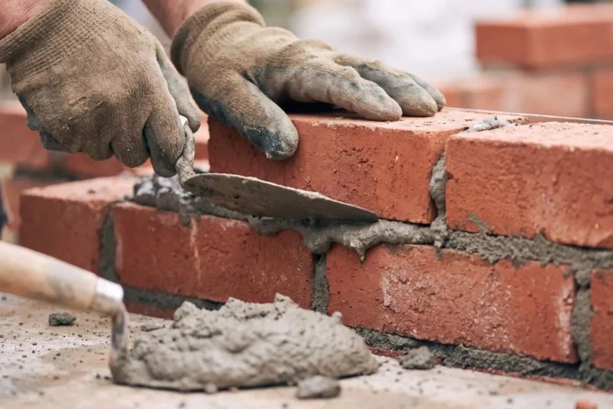 Albañil aplicando mortero con una llana durante la construcción de un muro de ladrillo.