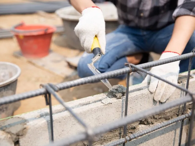 Trabajador aplicando mortero sobre bloques de concreto con estructura de acero de refuerzo.