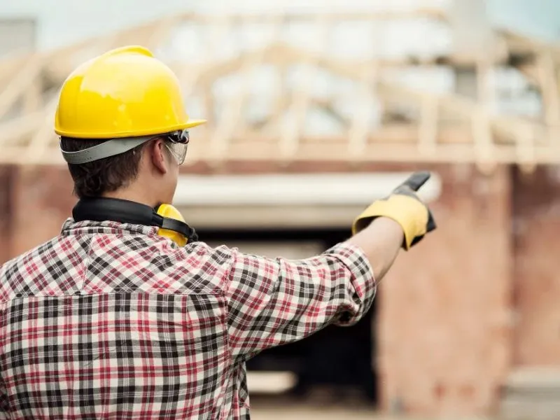 1. Trabajador de construcción con casco de seguridad supervisando una obra y señalando la estructura en construcción.