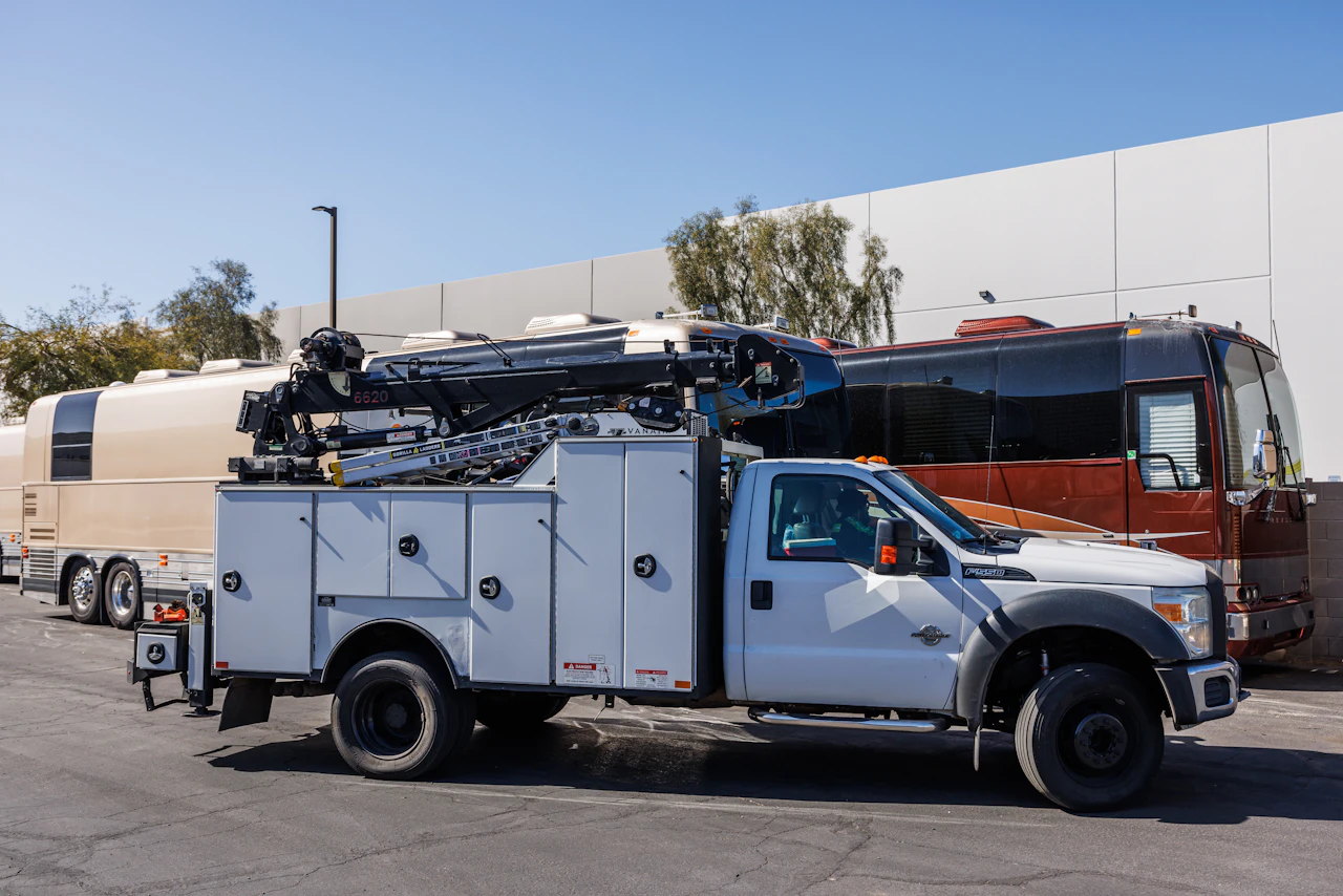A truck parked in a commercial lot, featuring a white service body with mounted crane boom and utility storage compartments