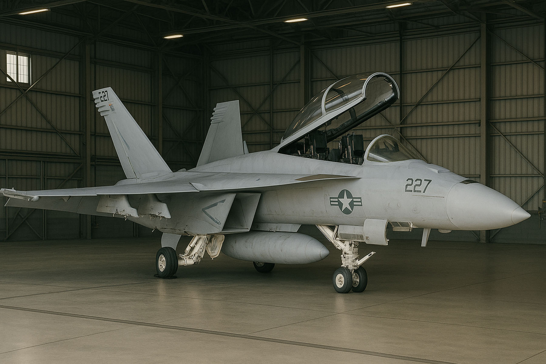 Gray F/A-18 Hornet fighter jet with open cockpit parked inside an aircraft hangar.