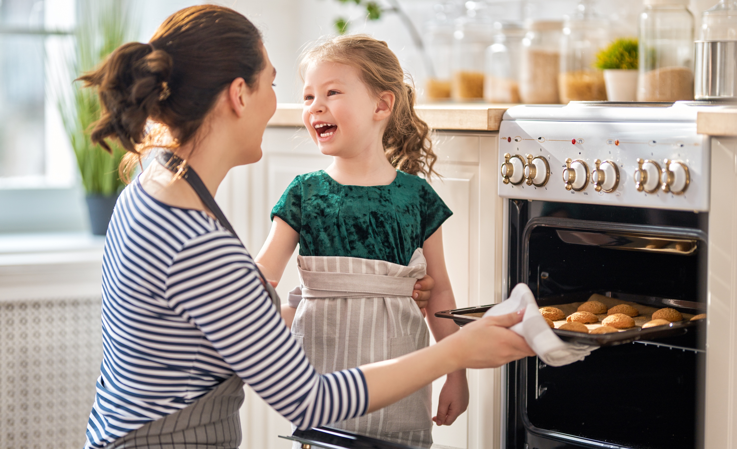 Daughter smiling at mother pulling cookies out of the oven