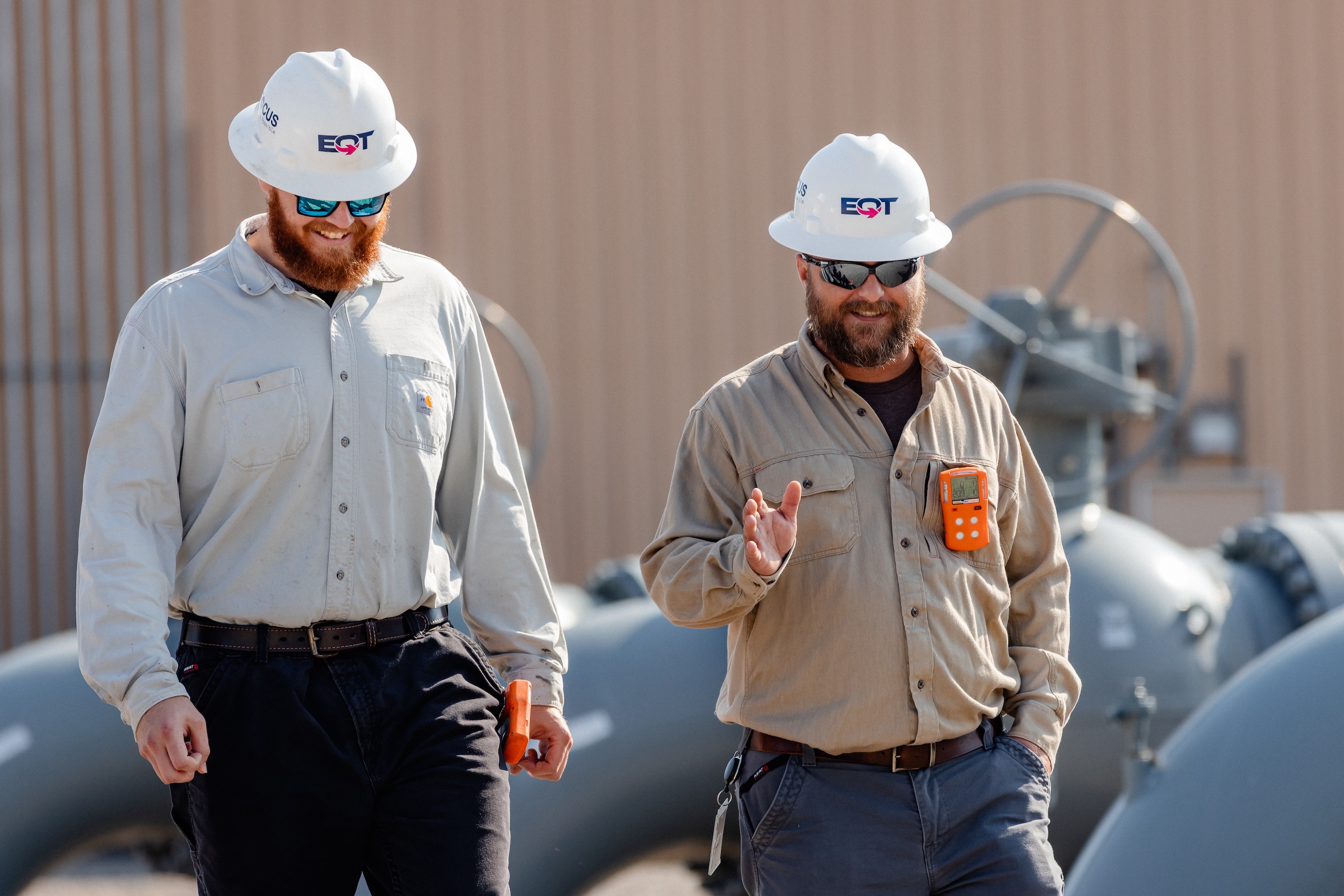 Two men in hard hats and safety gear talking on pipeline site